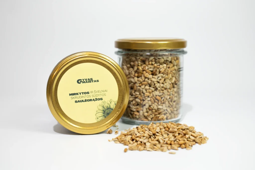 Jar of roasted salted sunflower seeds with a gold lid, seeds spilled in a small pile in front of it.